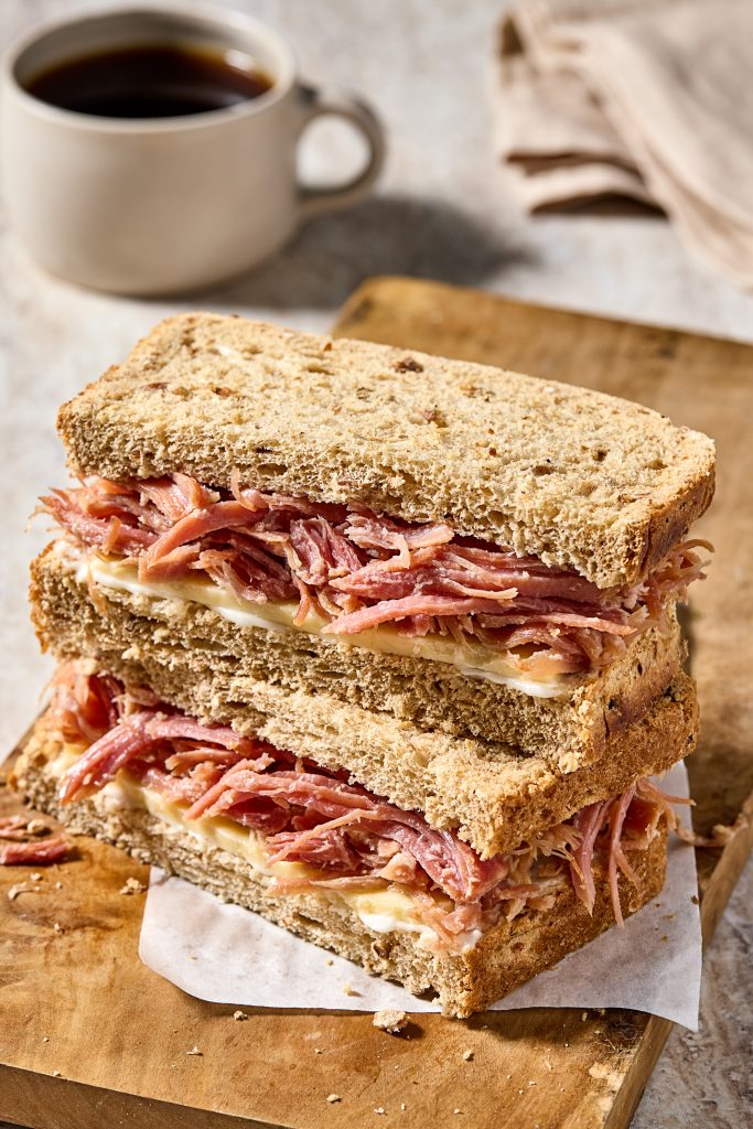 Rustic pulled meat and cheese sandwich on seeded bread with hot black coffee in a cosy setting.