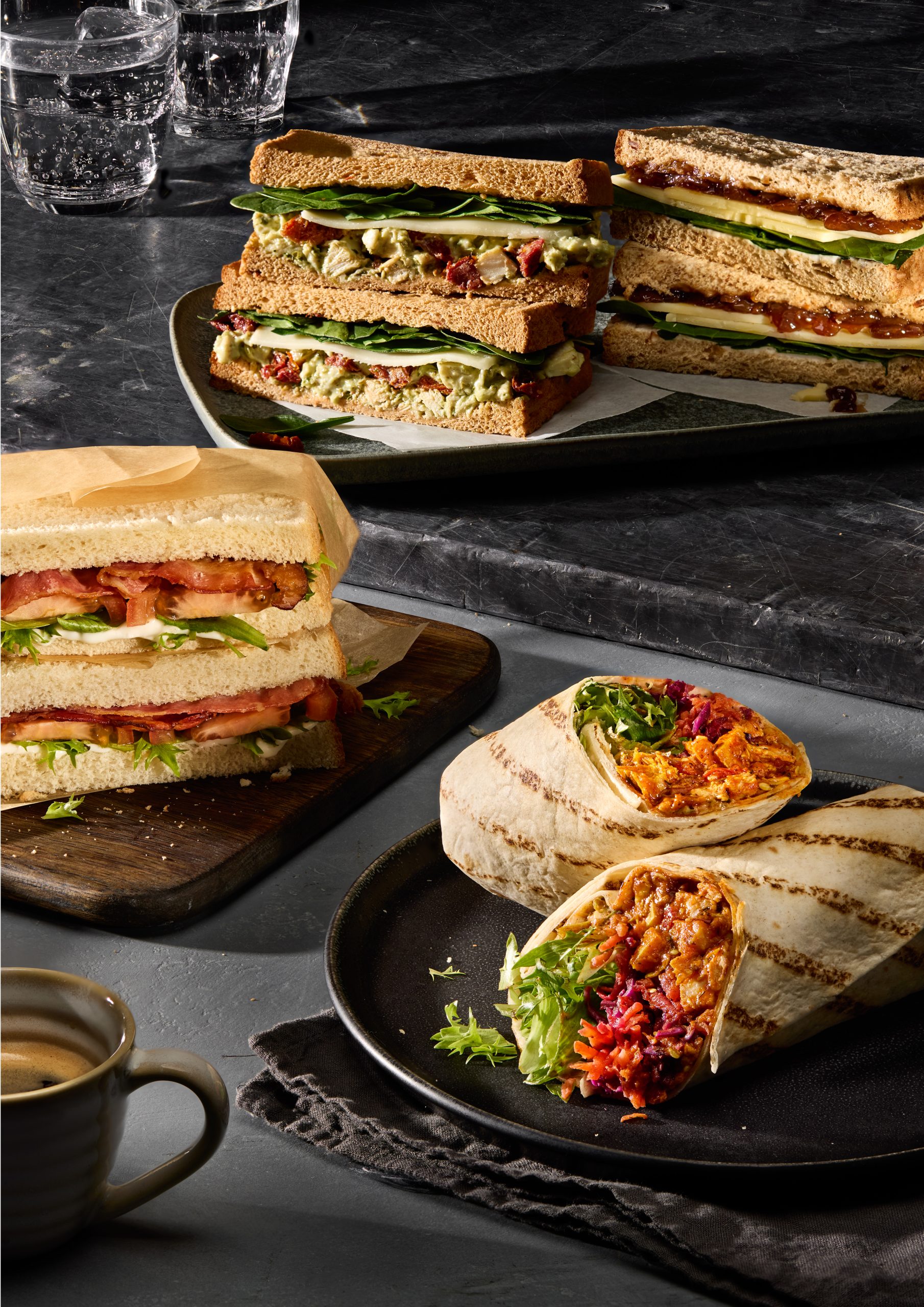 Assorted gourmet sandwiches and wraps with coffee on a dark platter, perfect for a modern brunch.
